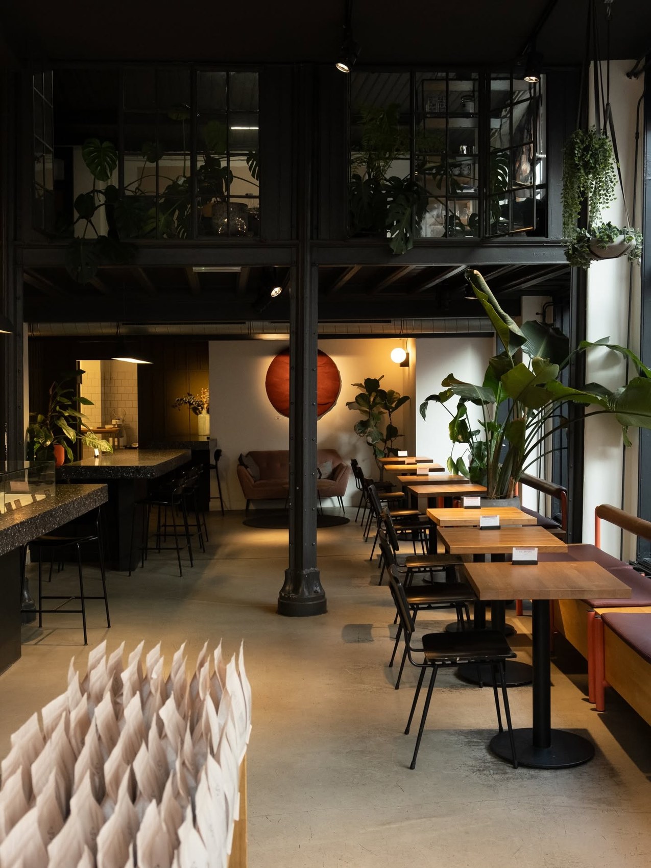 The two-level Single Estate interior, a mezzanine of plants over a ground floor dining room with wooden tables, a lounge corner and an industrial iron column